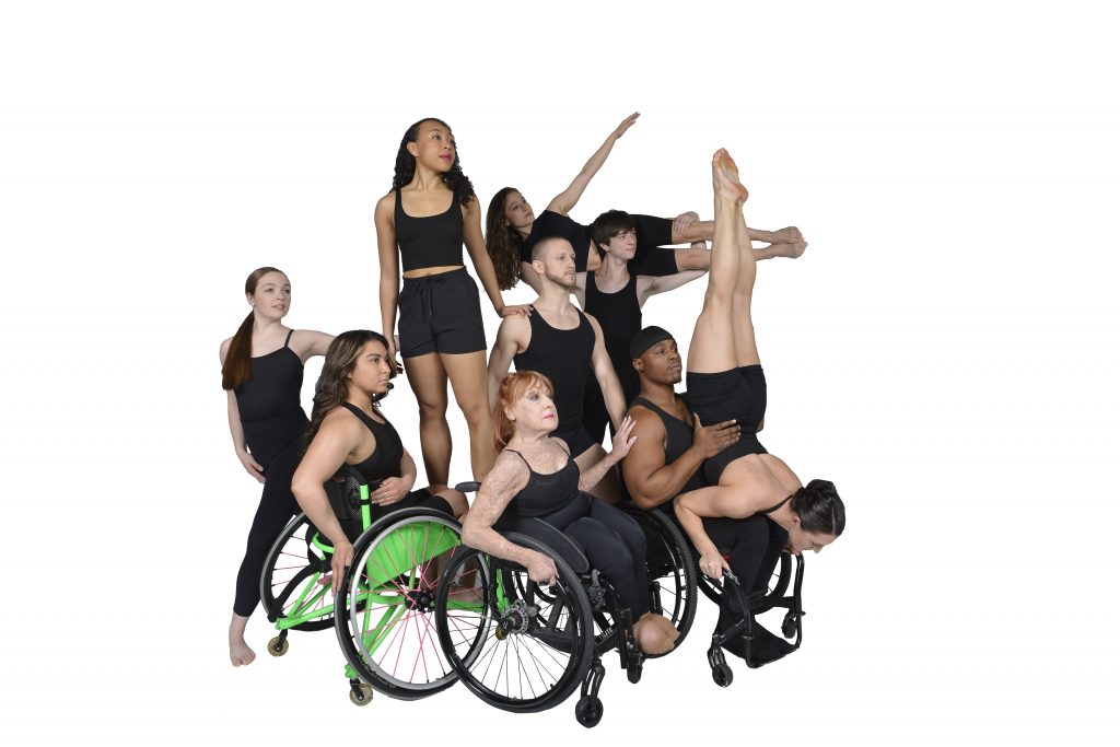 White background, dancers with and without disabilities posed holding on to each other