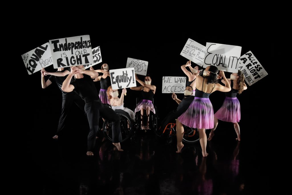 Dancers with and without disabilities face each other holding demonstration signs