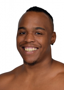 DeMarco Sleeper headshot smiling and looking at the camera, bare shoulders, dark skin, short black hair pulled back at the top of his head.