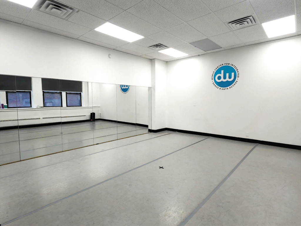 Image of a dance studio from the back left corner showing mirrors, a white wall, and a grey floor.